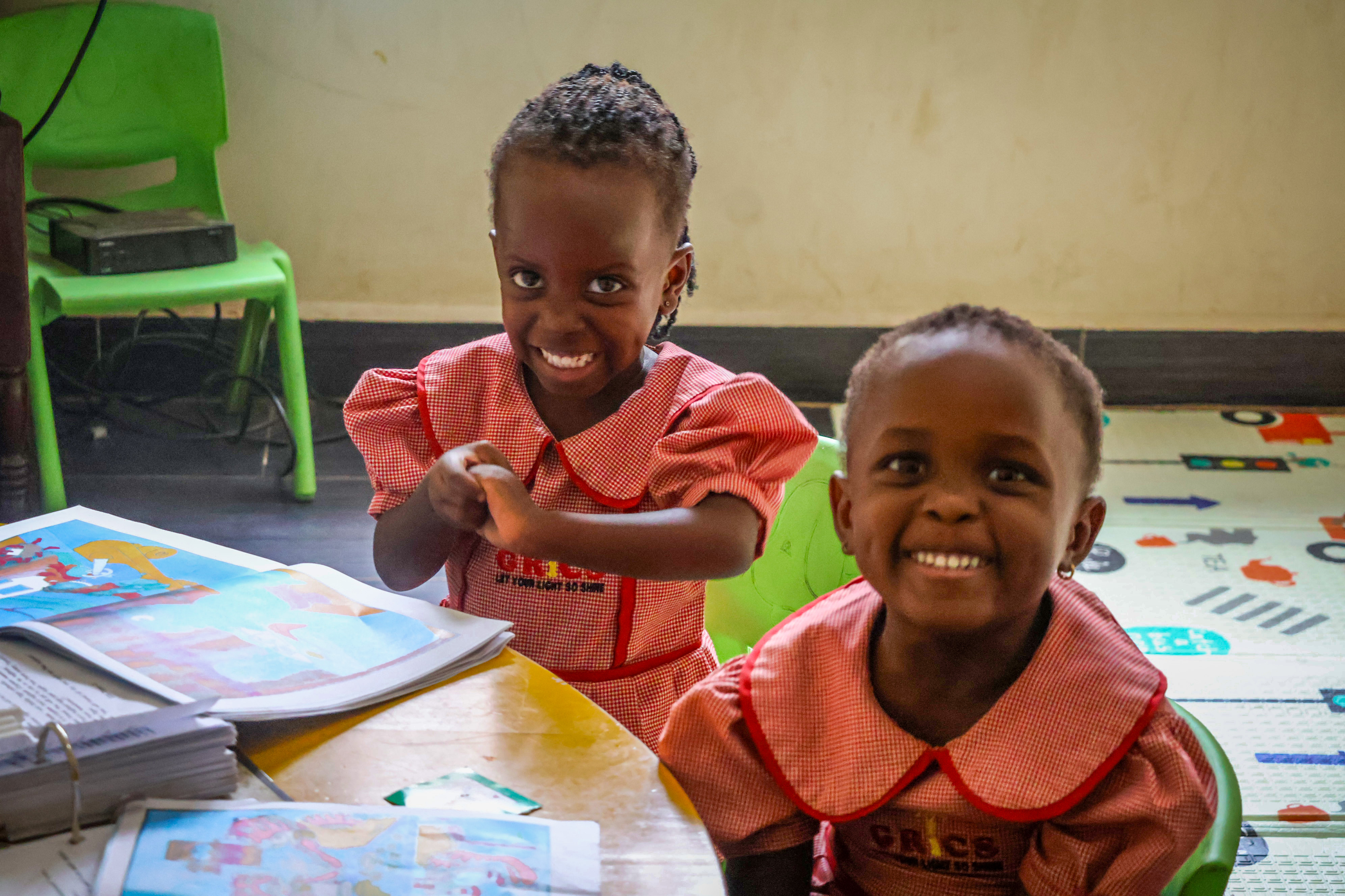 Two young GRICS learners smiling at their desk with storybooks